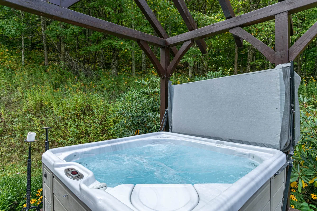 A serene outdoor hot tub nestled under a wooden structure, surrounded by lush greenery, inviting guests to relax while soaking in nature and views. The setting suggests a perfect spot for unwinding after adventures or socializing under the stars.