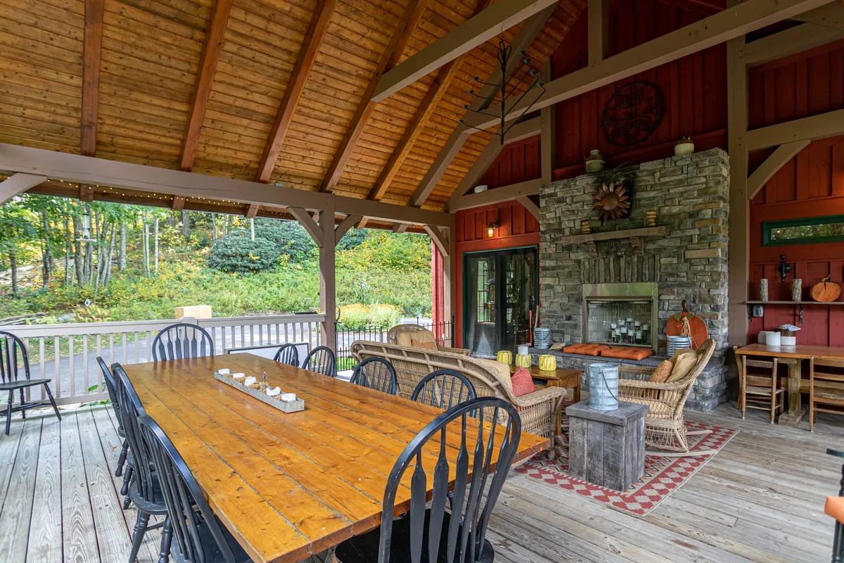An inviting covered outdoor dining area with a large wooden table, stone fireplace, and comfortable seating, accentuated by decorative accents. The space is ideal for group meals, evening storytelling, or celebrating special occasions in the mountain air.