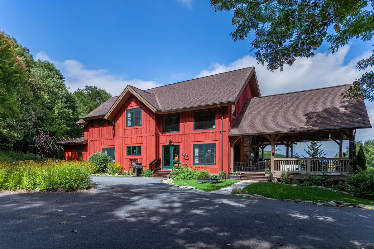 A charming red wooden home facade with a large, welcoming front porch and landscaped garden, embodying the warmth and inviting atmosphere of a mountain getaway. The porch suggests space for gatherings, while the garden sets a tranquil scene for group reunions.