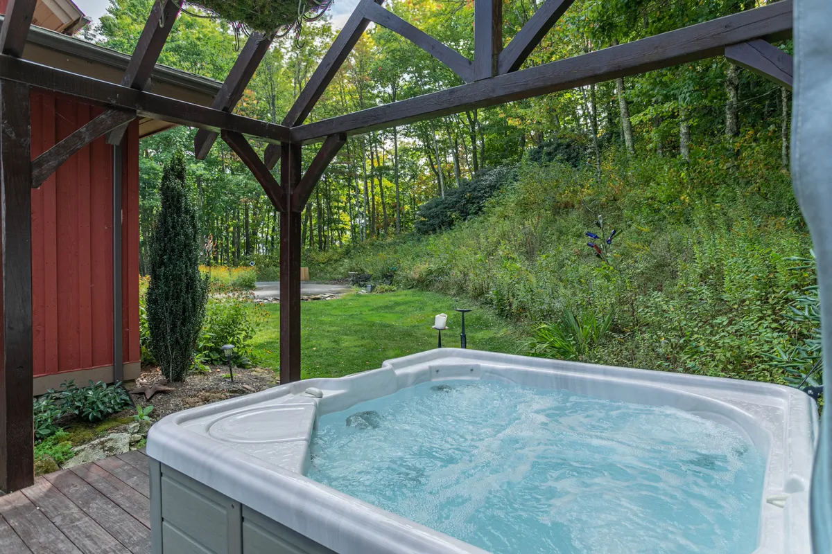 A serene exterior scene with a hot tub beneath a wooden pergola, surrounded by lush greenery. The relaxed vibe invites guests to enjoy sunsets, socialize, or simply unwind with nature all around.