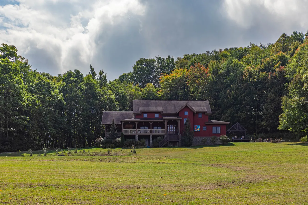 The red house nestled in a lush forest setting, with a welcoming porch and a spacious green lawn. The surrounding trees highlight the seclusion and connection to nature, while the open lawn and porch suggest space for group activities and relaxation.