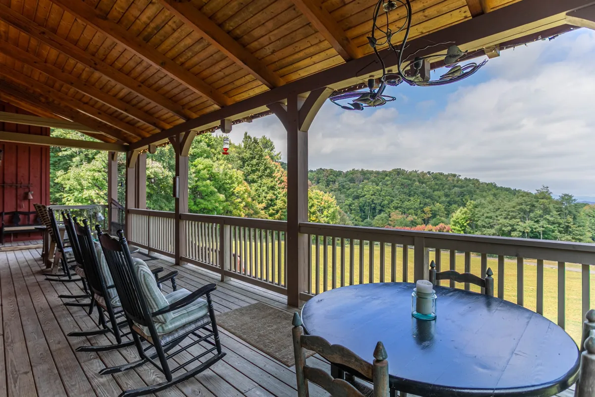 A covered porch with classic rocking chairs and a round table, set against a backdrop of rolling green hills and trees. The porch offers a tranquil spot to relax and enjoy the serene mountain landscape, perfectly suited for unwinding after a day outdoors.