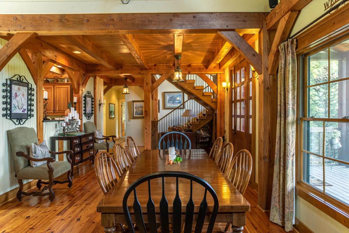 This interior shot highlights a spacious wooden dining table beneath exposed beams, with large windows letting in natural light. The space feels communal and adaptable, ideal for group gatherings or multi-family getaways, and echoes the rustic-meets-modern aesthetic.