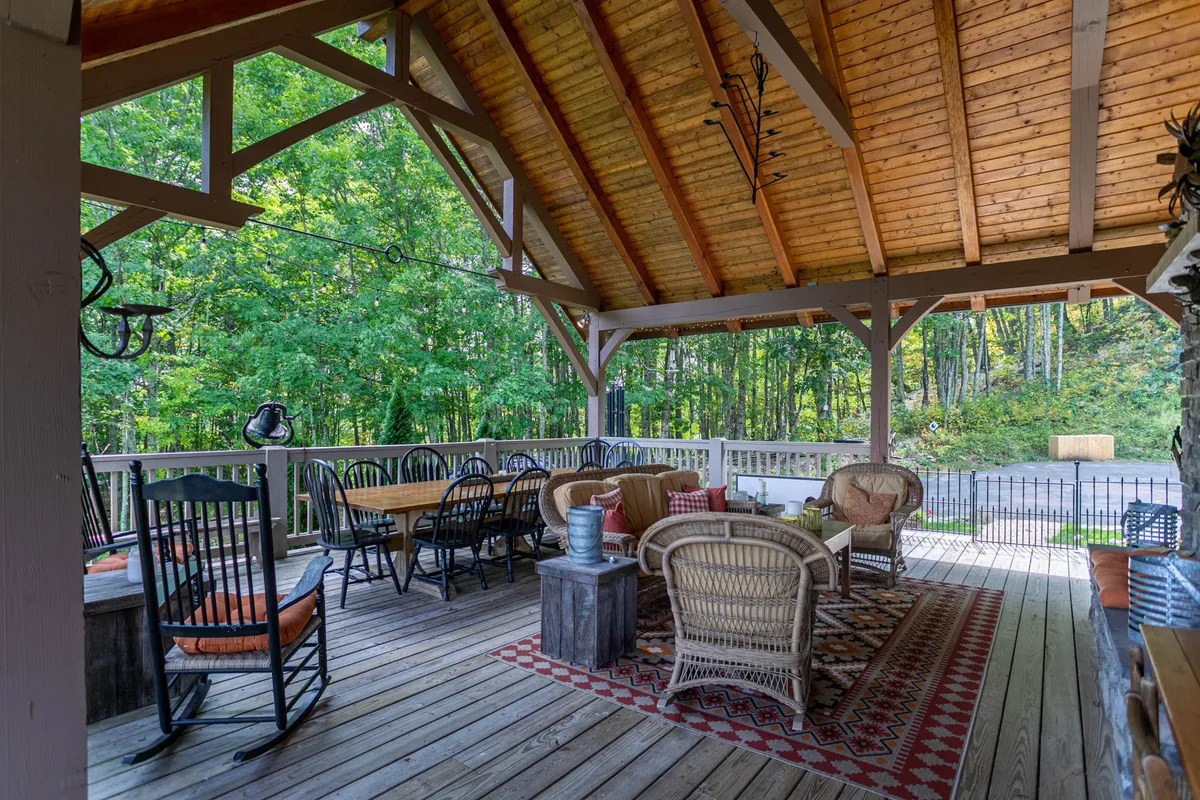 A welcoming porch featuring classic wooden rocking chairs, a dining table set for meals, comfortable woven furniture, and a decorative rug. The porch is oriented to catch the warm glow of sunset or the soft light of early morning, with open views into the natural surroundings.