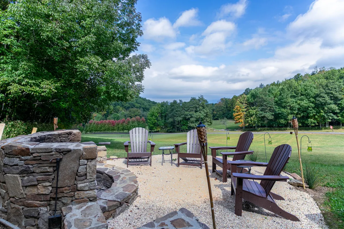 A cozy outdoor fire pit area with sturdy stonework, wooden Adirondack chairs, and a gravel circle set amidst trees. This seating area is ideal for gathering at dusk, sharing stories, roasting marshmallows, or simply enjoying the untouched tranquility of the outdoors.