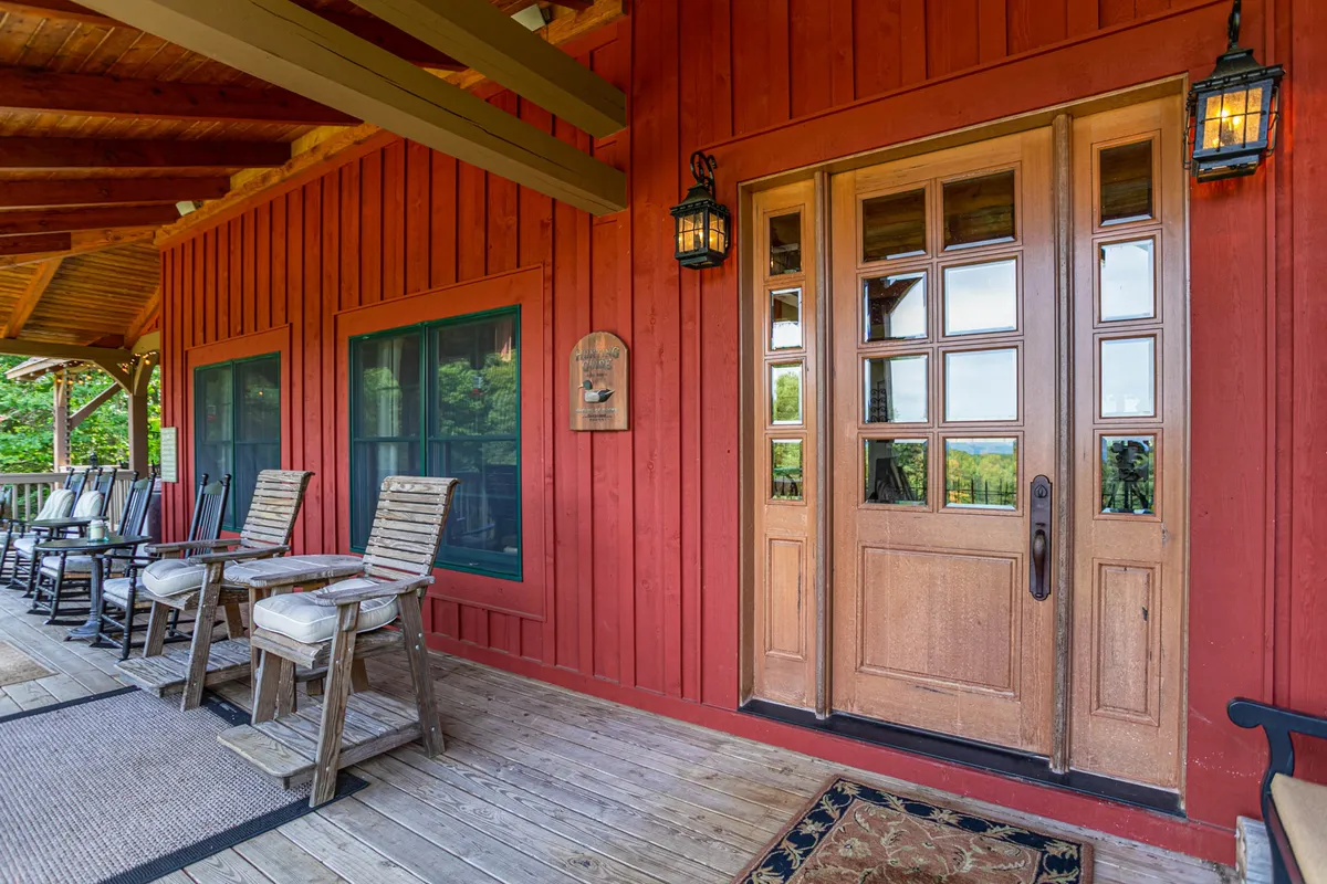 This exterior image showcases the inviting front porch with a wooden door, decorative lanterns, and a comfortable sitting area with chairs against the red wooden siding. The setting hints at amenities just outside (like the EV charger and security features) and demonstrates the welcoming, pet-friendly atmosphere.
